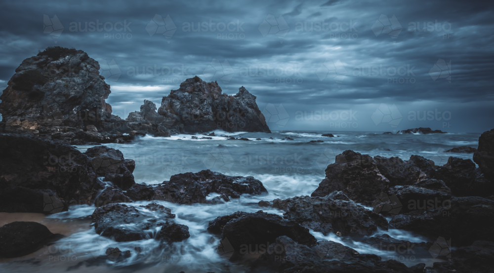 camel rock bermagui with dark storm clouds over rocks on ocean shore - Australian Stock Image