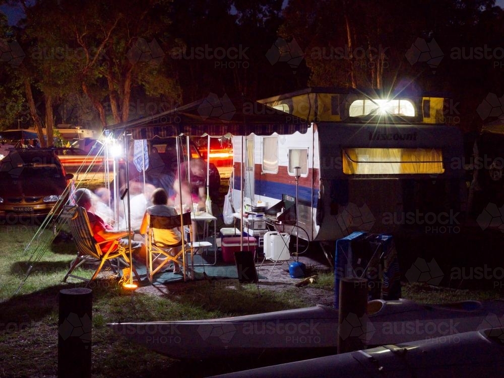 Campers relaxing at night outside a caravan - Australian Stock Image