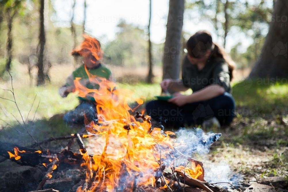 Campfire flames with out of focus people eating behind - Australian Stock Image