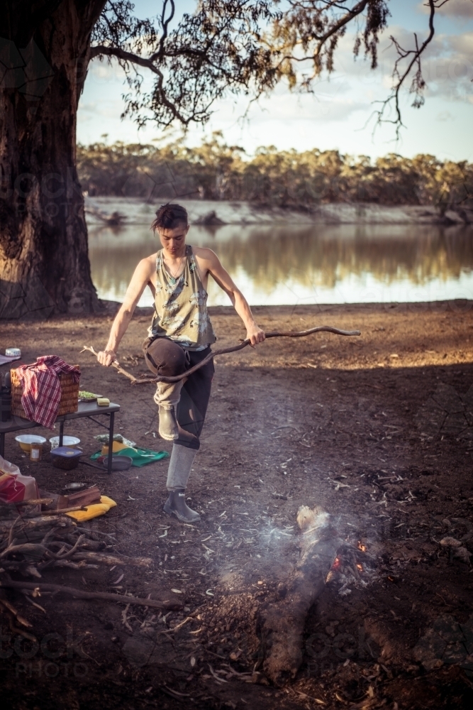 Camping life - female breaking a large stick against her knee to put on the camp fire - Australian Stock Image