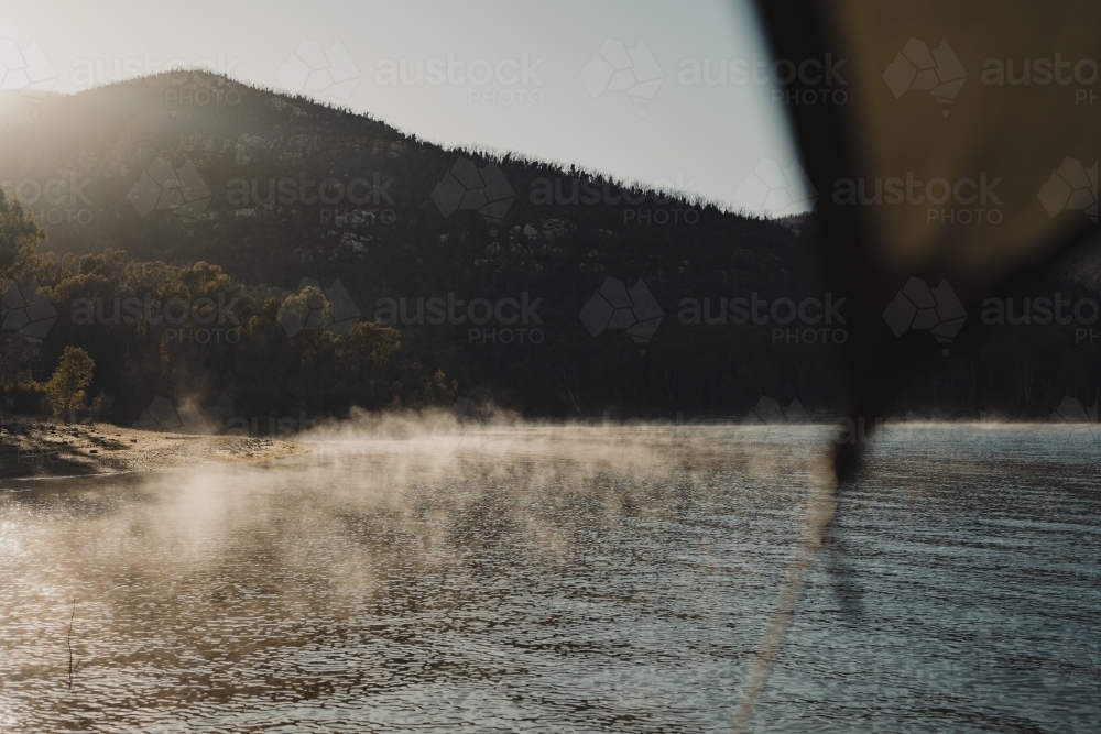 Campsite views. Morning fog lit up by the sun with mountains in the background - Australian Stock Image