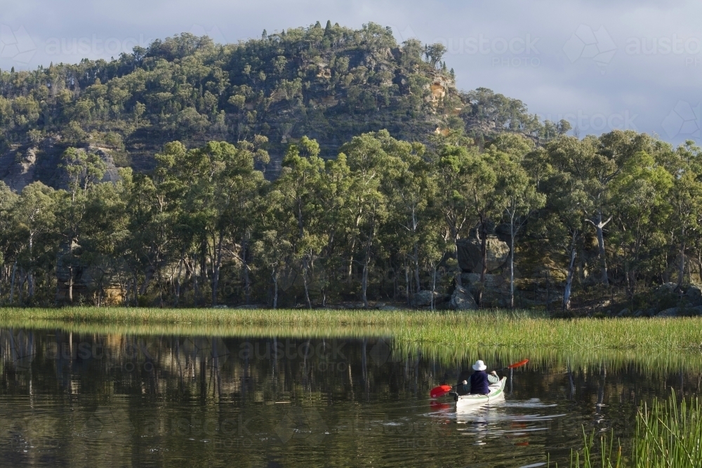 Canoeing on dam with reeds, cliffs and bushland - Australian Stock Image