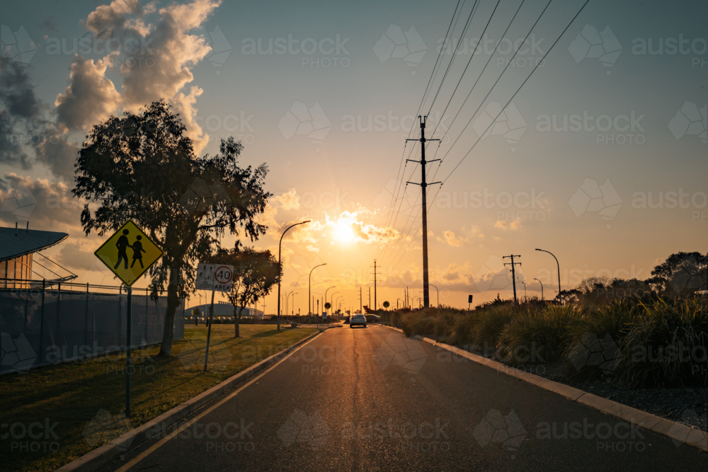 Car driving into vibrant sunset along small town street - Australian Stock Image