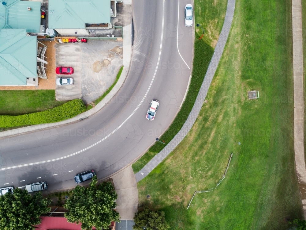 Car driving on curved corner bend in road in town from above - Australian Stock Image