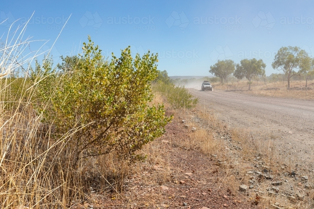 car in distance driving down dusty unsealed road - Australian Stock Image