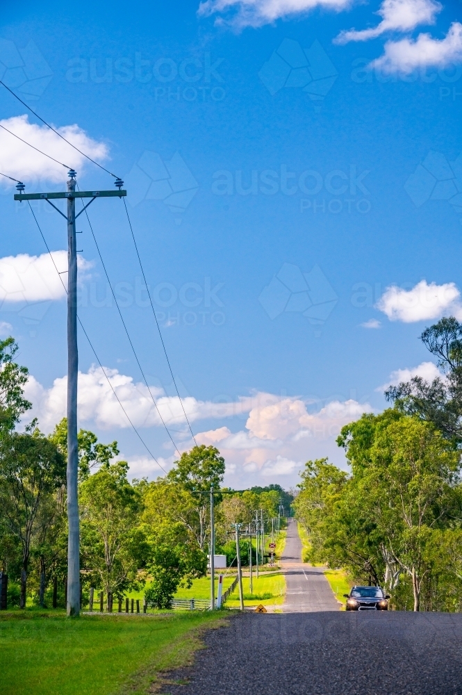 Car on asphalt country road (Schilling Road, Calliope) with telephone poles and lines - Australian Stock Image