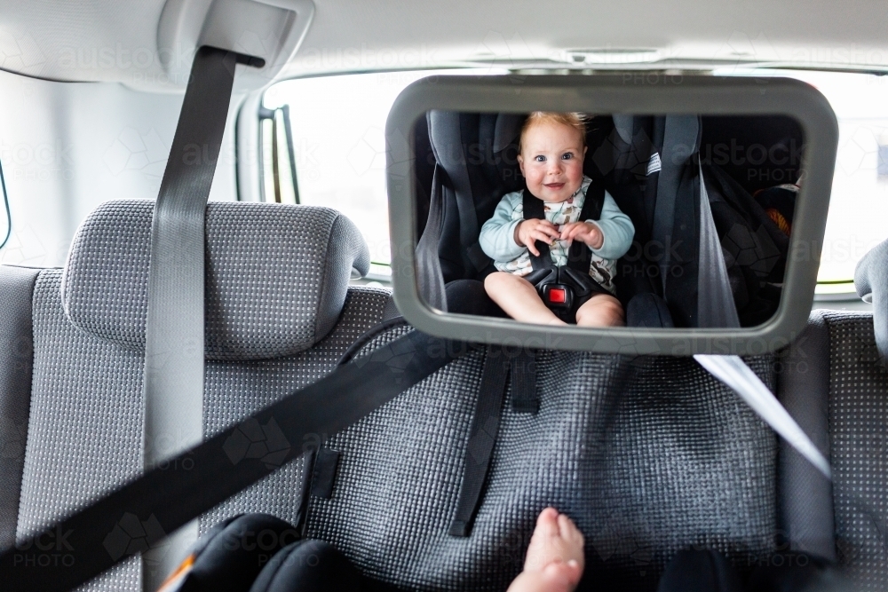 Car seat mirror with happy baby face reflected in rear facing infant seat - Australian Stock Image