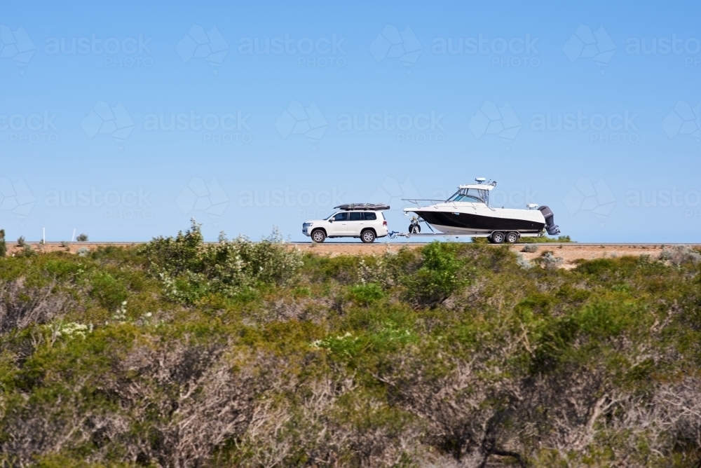 Car towing a boat along a coastal road in Western Australia under blue sky, with motion blur. - Australian Stock Image