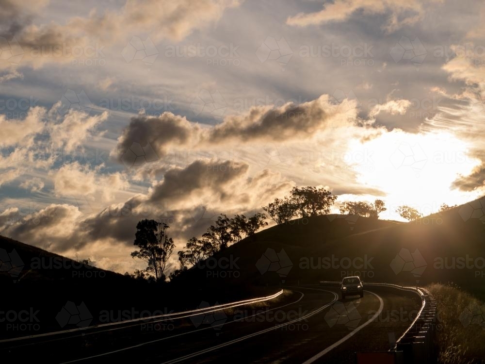 Car travelling on a curve silhouetted against the late afternoon sun - Australian Stock Image