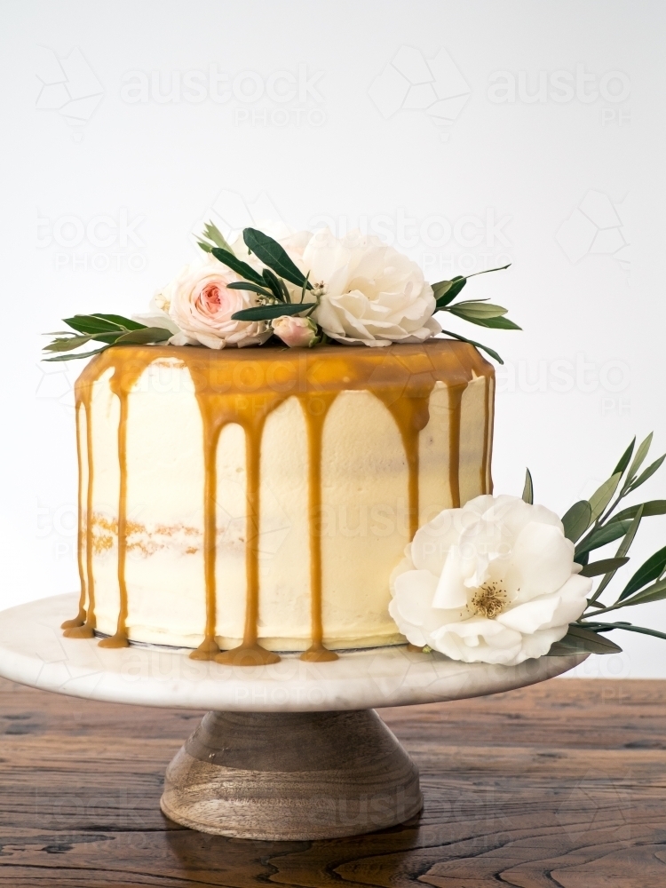 Caramel drip layer cake on cakestand with flowers - Australian Stock Image