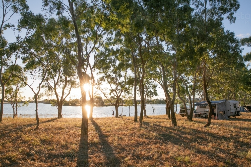 Caravan by a lake with long shadows in the late afternoon light and person walking. - Australian Stock Image