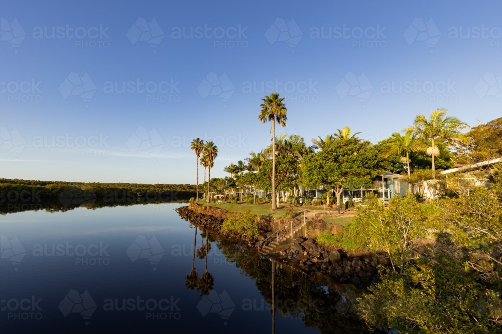 Caravan park beside Brunswick River with tall palm trees reflected in water - Australian Stock Image