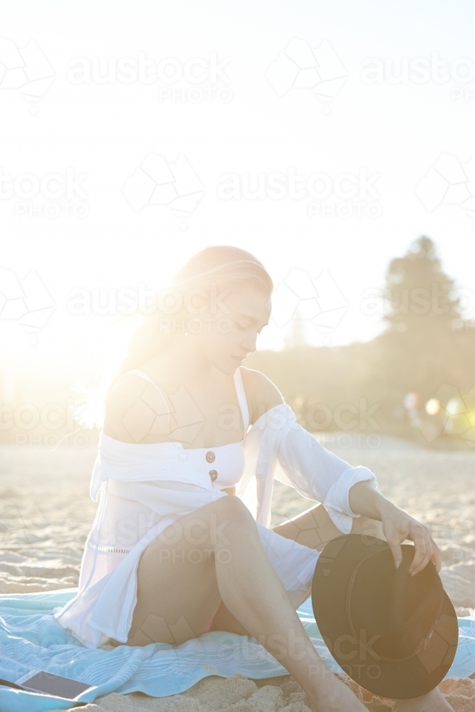 Carefree young blonde-haired woman at beach with black hat - Australian Stock Image