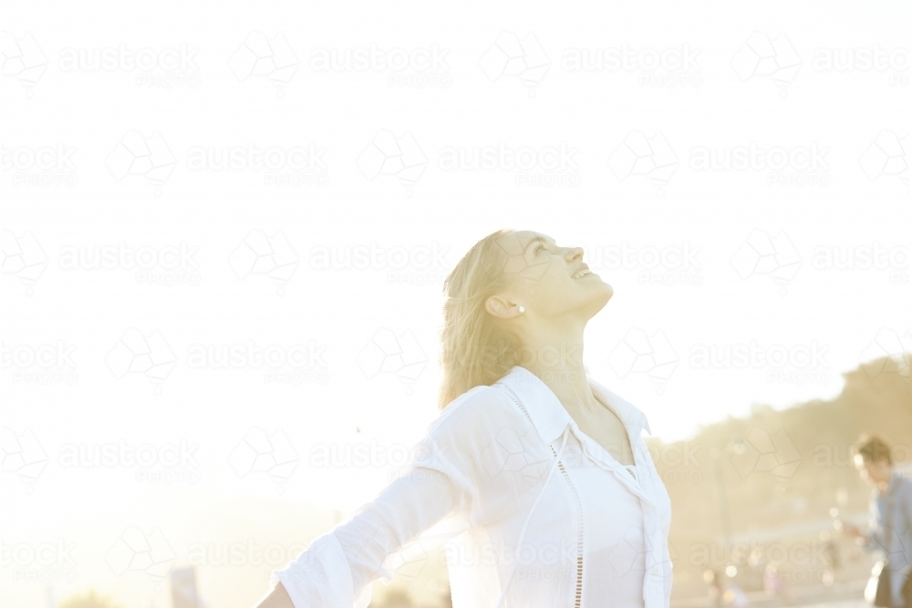 Carefree young blonde-haired woman at beach with arms out-stretched enjoying the sunshine - Australian Stock Image