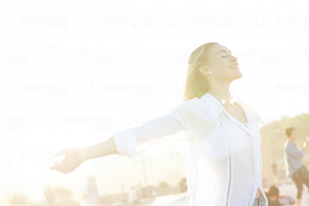 Carefree young blonde-haired woman at beach with arms out-stretched enjoying the sunshine - Australian Stock Image