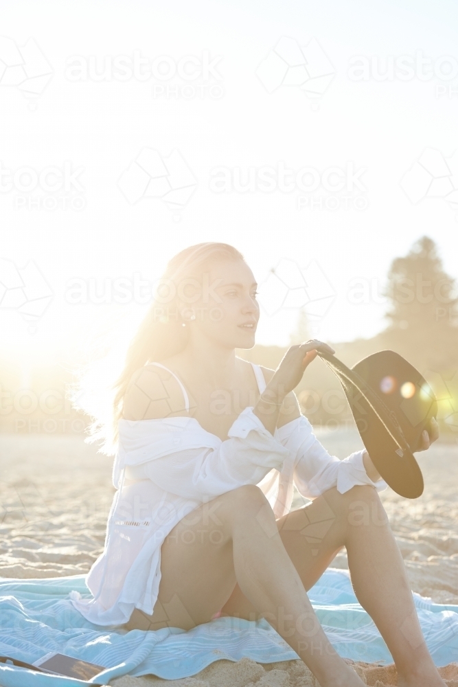 Carefree young blonde-haired woman at beach with black hat - Australian Stock Image