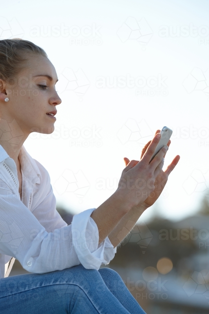 Carefree young blonde-haired woman checking mobile phone - Australian Stock Image