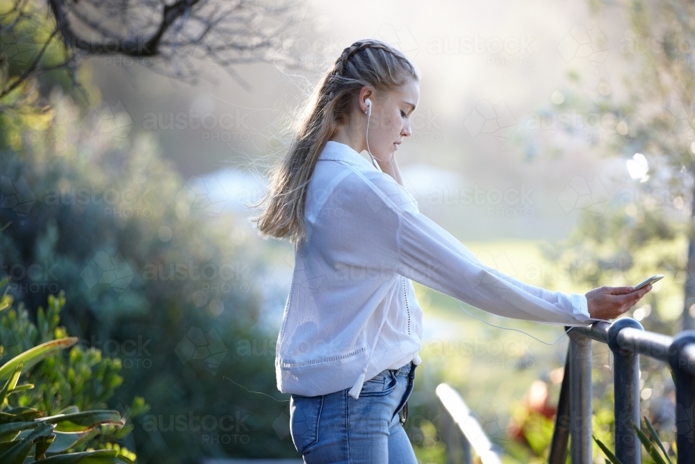 Carefree young blonde-haired woman listening to music with headphones outdoors - Australian Stock Image