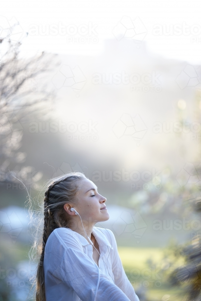 Carefree young blonde-haired woman listening to music with headphones outdoors - Australian Stock Image