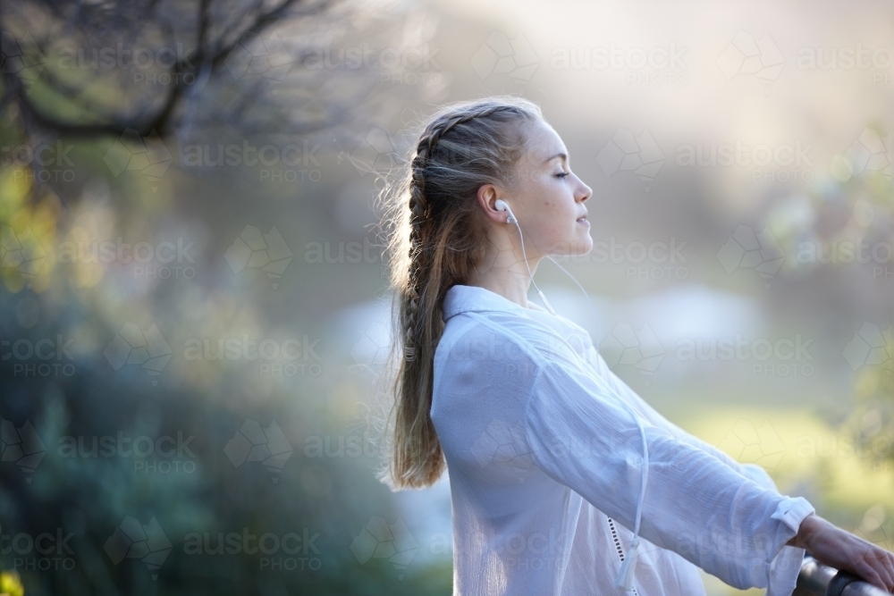 Carefree young blonde-haired woman listening to music with headphones outdoors - Australian Stock Image
