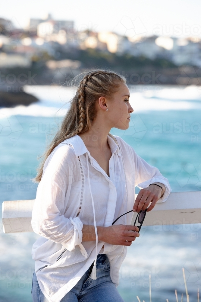Carefree young blonde-haired woman looking out over ocean - Australian Stock Image