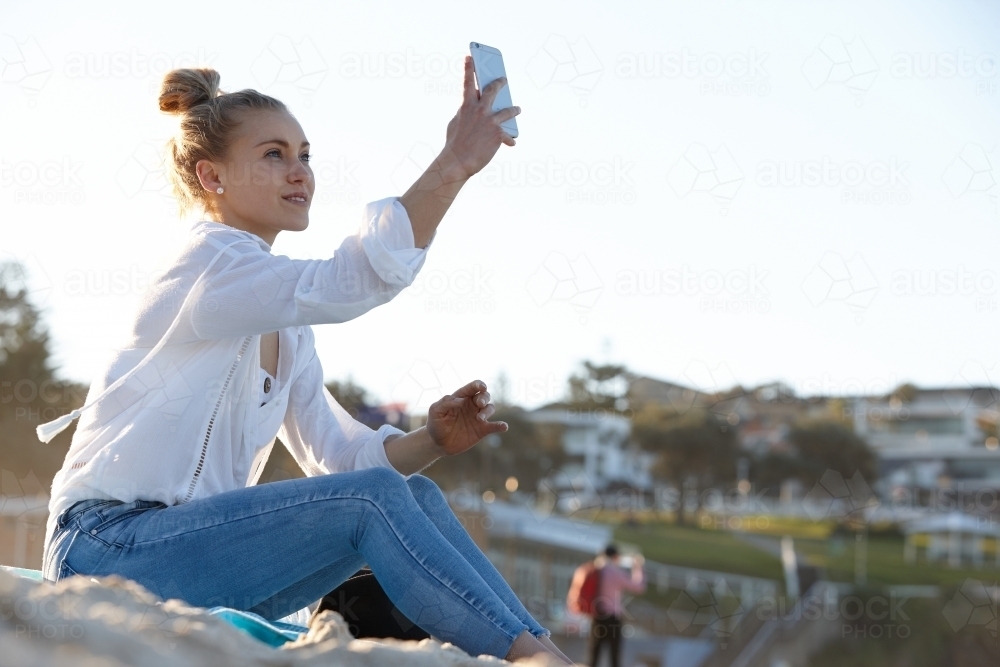 Carefree young blonde-haired woman taking a selfie at beach - Australian Stock Image