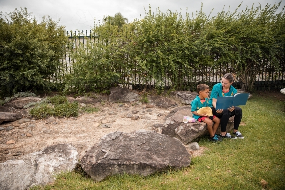 Carer reading with young boy outside - Australian Stock Image
