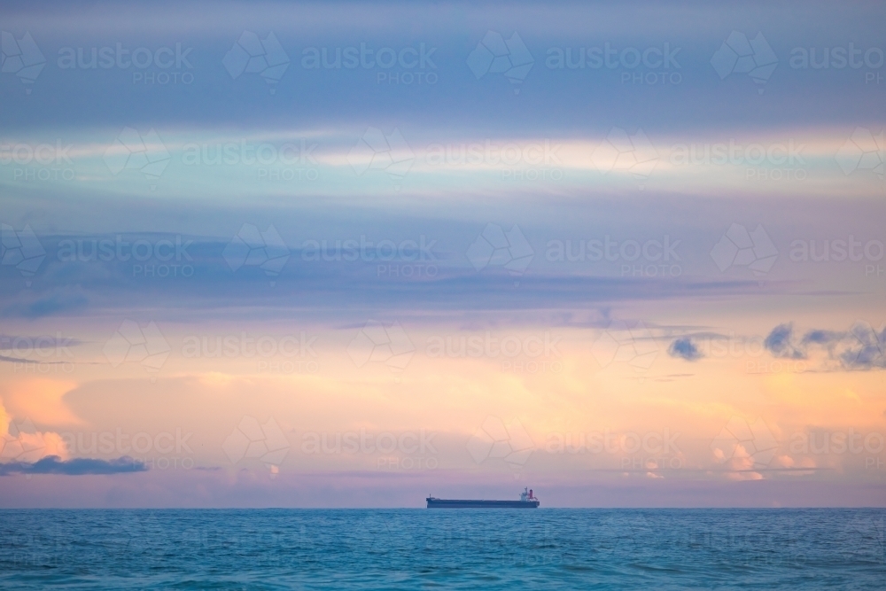 Cargo ship lined up at sea en route to Newcastle Harbour under a vibrant sunset sky - Australian Stock Image