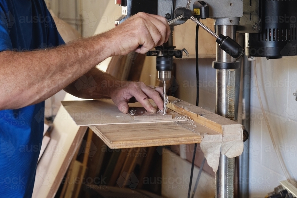 Carpenter using vertical drilling machine in woodwork workshop - Australian Stock Image