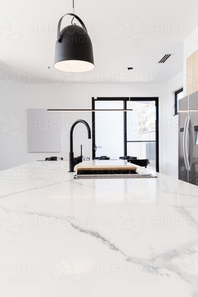 Carrara marble benchtop with black gooseneck kitchen tap and black pendant - Australian Stock Image