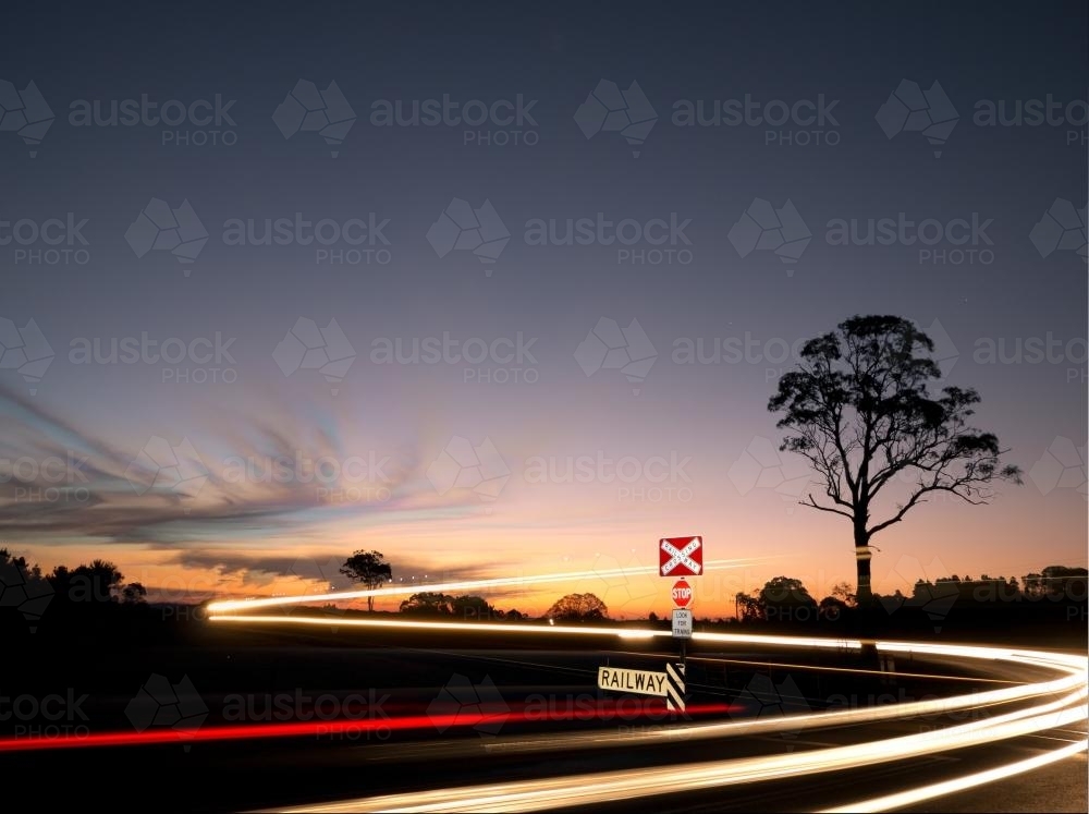 Cars and train light trails at a railway crossing at night - Australian Stock Image