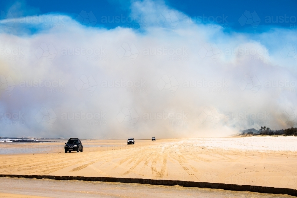 Cars driving along eastern beach of Fraser Island with bushfire smoke in the background - Australian Stock Image