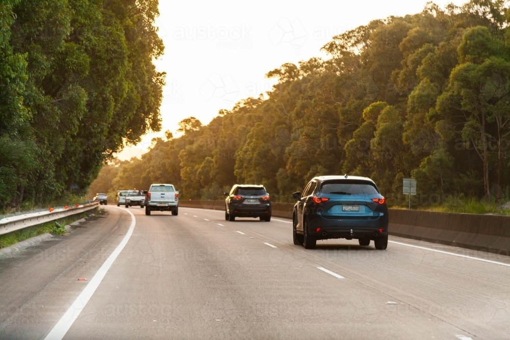Cars driving down highway road overtaking one another at sunset - Australian Stock Image