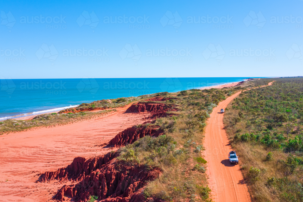 Cars driving on remote red dirt road by the sea - Australian Stock Image