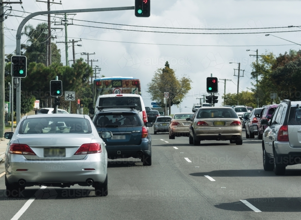 Cars driving through traffic lights on busy urban street in daytime - Australian Stock Image