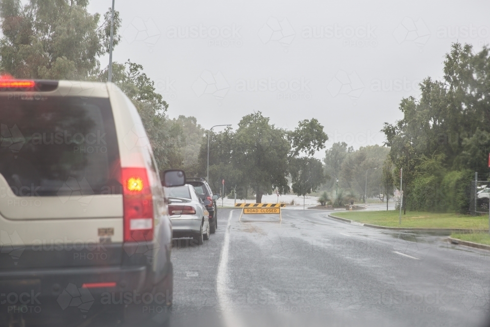 Cars lined up on road with road closed sign due to flooding - Australian Stock Image