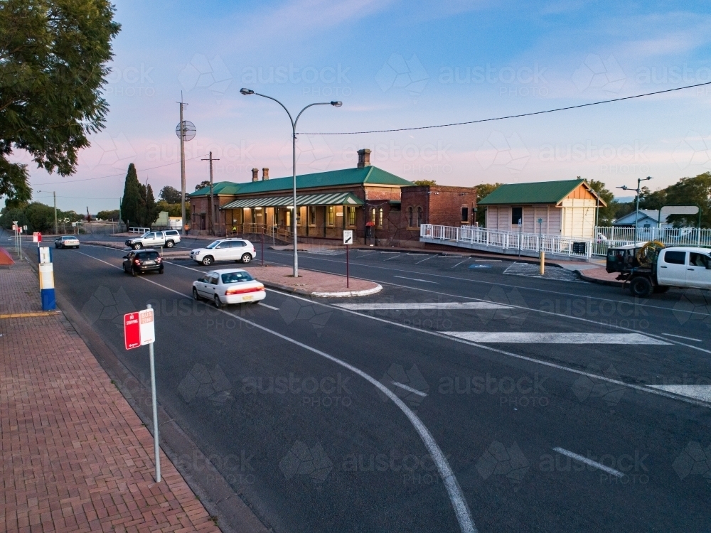 cars on road passing bus stop and train station in country town at dusk - Australian Stock Image