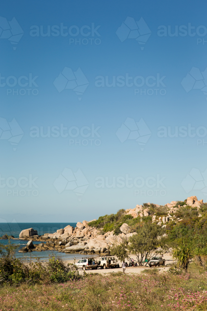 Cars parked on beach with grass and rocks in the afternoon - Australian Stock Image