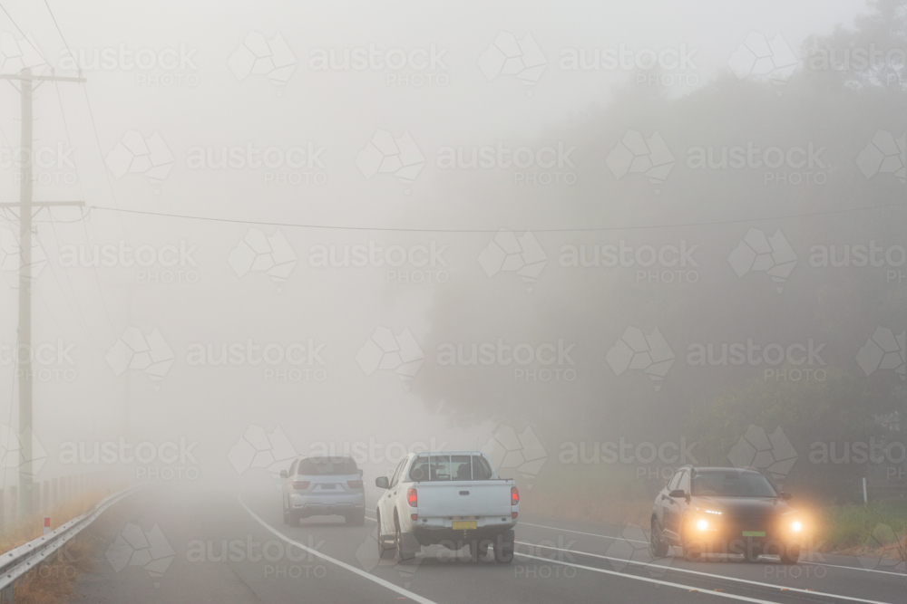 Cars travelling on highway road through fog with low visibility - Australian Stock Image