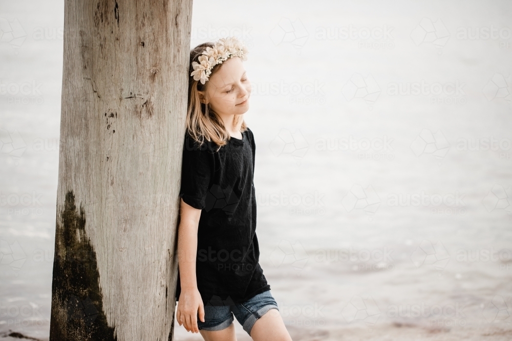 Caucasian girl standing underneath a pier at the beach wearing a flower head band - Australian Stock Image