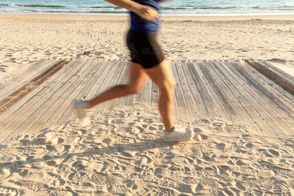 Caucasian woman jogging on sandy beach boardwalk - Australian Stock Image