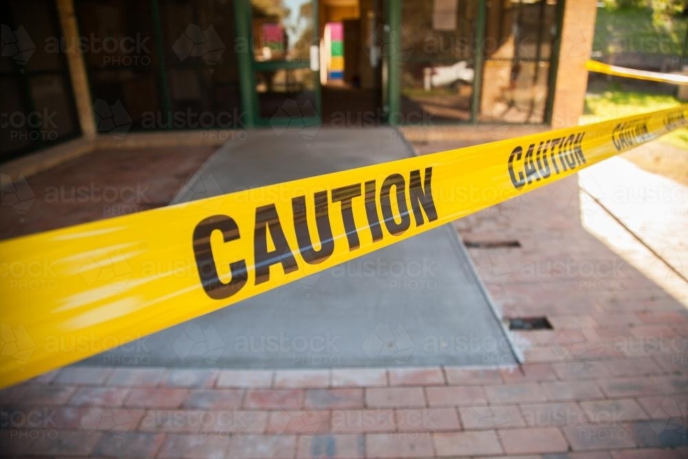 Caution tape stopping people walking on wet concrete ramp - Australian Stock Image