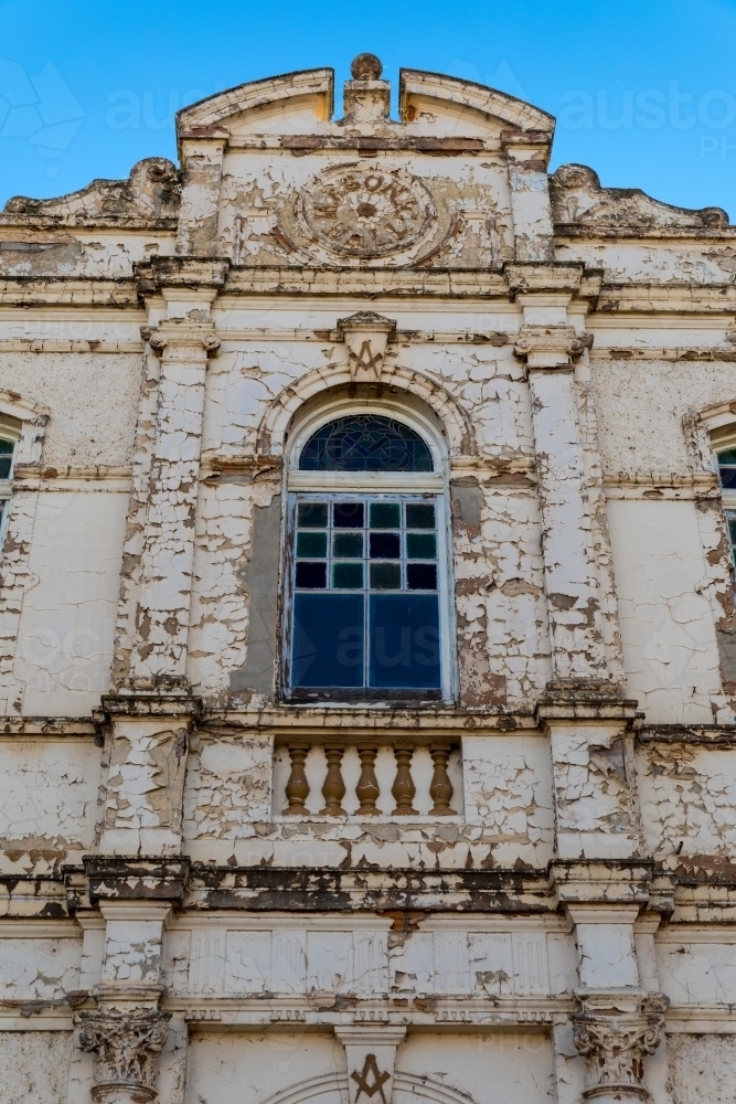 Center window of an old derelict building with weathered facade standing grand against a blue sky - Australian Stock Image