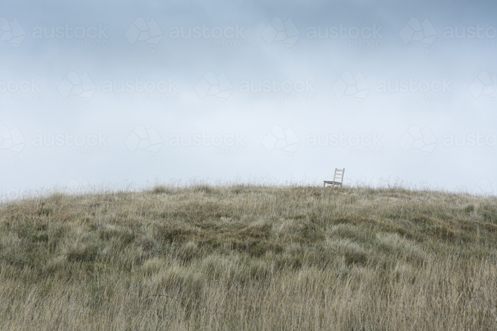 Chair on grassy hill with grey sky - Australian Stock Image