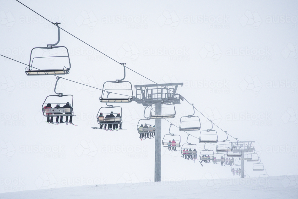 Chairlift with lots of skiiers on, going up mountain in the mist - Australian Stock Image