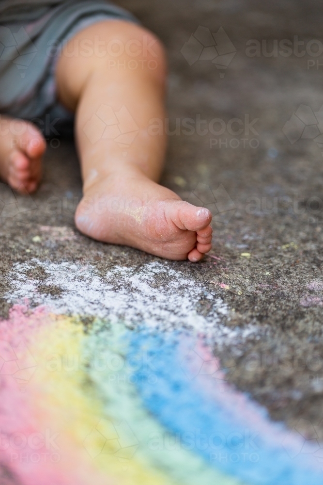 Chalk covered foot of child on concrete with colourful drawing - Australian Stock Image