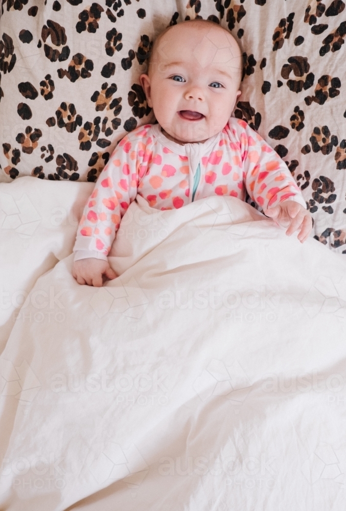 Cheeky little baby girl smiling from the bed. - Australian Stock Image