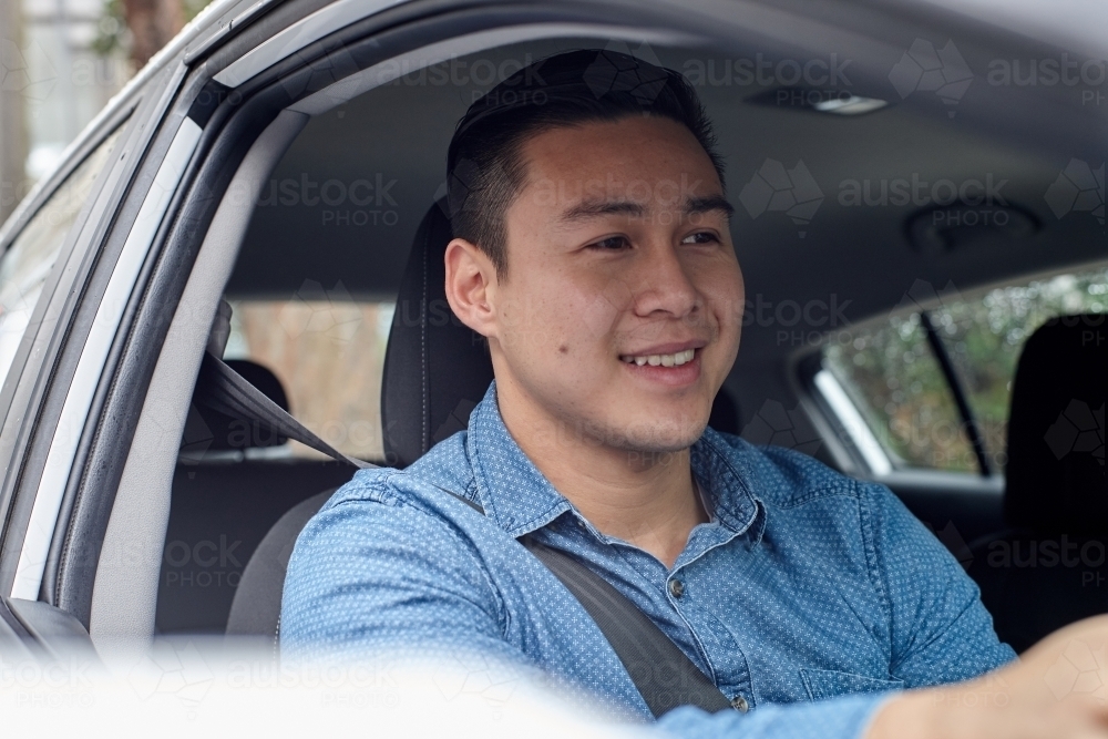 Cheerful Asian man driving in car - Australian Stock Image