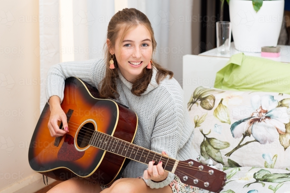 Cheerful teenager playing guitar in bedroom - Australian Stock Image