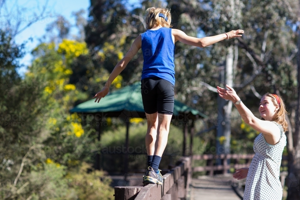 Child balancing and walking along fence with sister standing nearby - Australian Stock Image